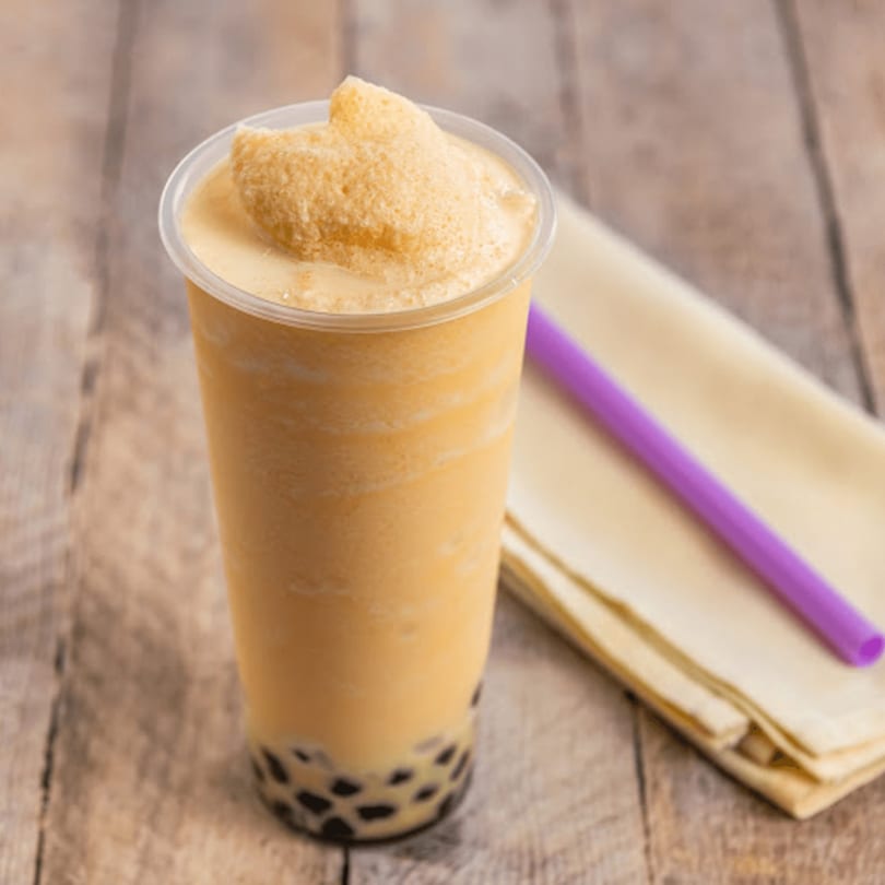 Nara Teriyaki and Pho's mango boba tea with tapioca pearls and a purple straw on a wooden table.