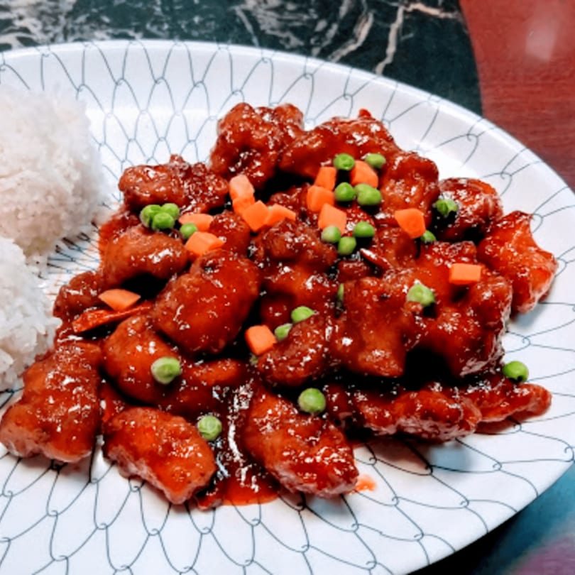 Sweet and sour chicken with peas and carrots, served with white rice on a patterned plate.