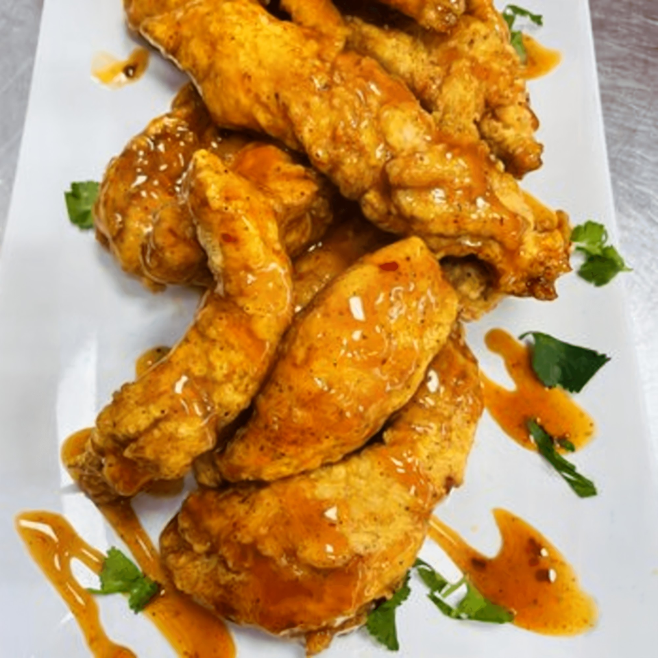 Crispy fried chicken tenders drizzled with a sweet and spicy sauce, garnished with fresh cilantro.
