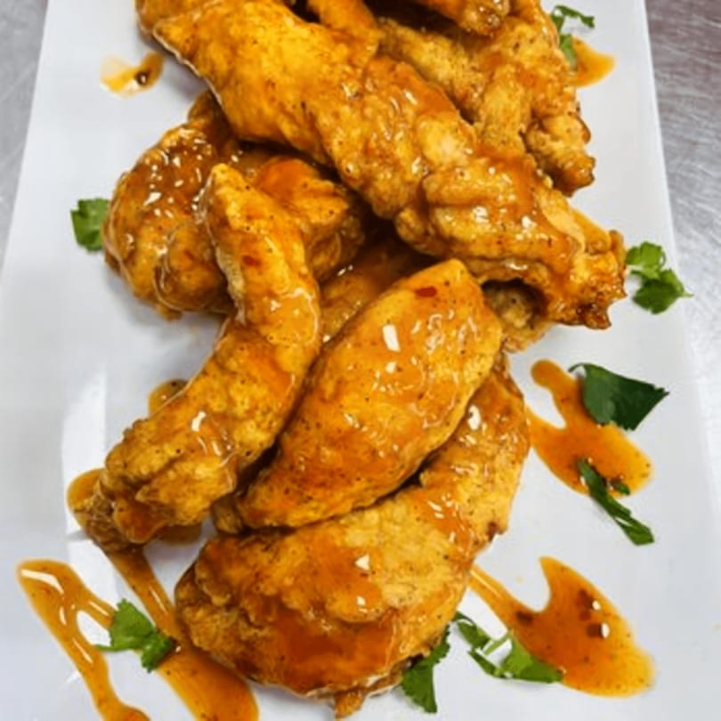 Crispy fried chicken tenders drizzled with a sweet and spicy sauce, garnished with fresh cilantro.