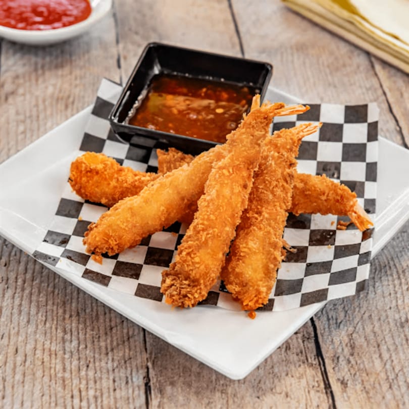 Crispy fried shrimp with a side of sweet chili dipping sauce on a checkered paper liner.