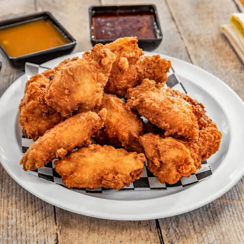 Crispy fried chicken wings on a white plate with checkered paper, served with two dipping sauces.